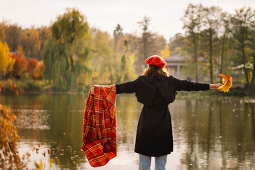 A Teengirl in a red beret with a bouquet of autumn leaves in her hands walks on wooden pontoon. Autumn mood. Autumn concept. Autumn day. Back view