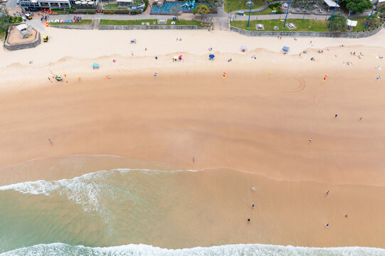 Aerial view of people on a wide sandy beach in front of waterfront parkland