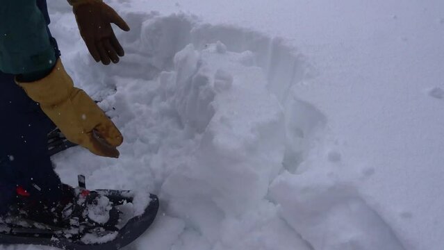 Man Cutting out a Block of Snow with a Shovel in order to Build a Shelter in the French Alps under Heavy Snowfall
