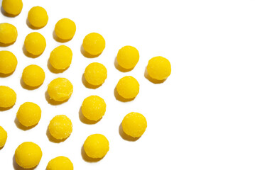 a lot of yellow round candies are laid out in a row on a white background on top of the frame, in perspective. selective focus. close-up
