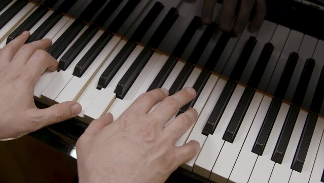 A Caucasian male is playing the piano. Camera angle is over the shoulder at a diagonal. Slow motion.