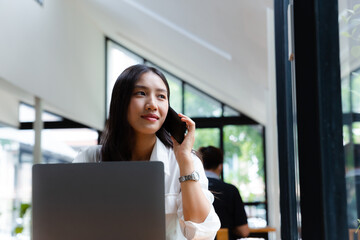 Young businesswoman talking on smartphone with her work at her desk in office.