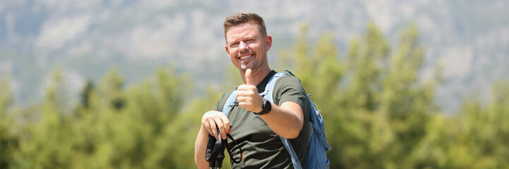 Fototapeta premium Man with Finnish sticks for Nordic walking holds thumbs up on mountain