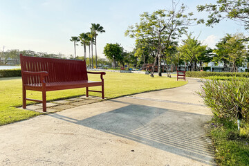 Wooden bench with long line of shadow on walking pathway in small peaceful park with green lawn and palm trees on beautiful summer tropical sunlight.