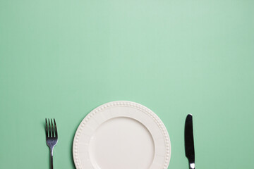 An empty plate with knife and fork over the green background. 
