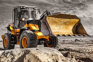 Powerful bulldozer or loader moves the earth at the construction site against the sky. An...