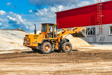 A large front loader pours sand into a pile at a construction site. Transportation of bulk materials. Construction equipment. Bulk cargo transportation. Excavation.