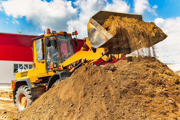 A large front loader pours sand into a pile at a construction site. Transportation of bulk...