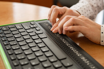 A blind woman uses a computer with a Braille display and a computer keyboard. Inclusive device. - obrazy, fototapety, plakaty