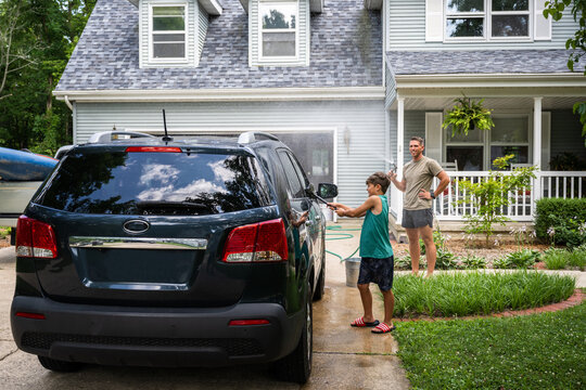 Air Force service member washes his vehicles with his sons in the driveway.