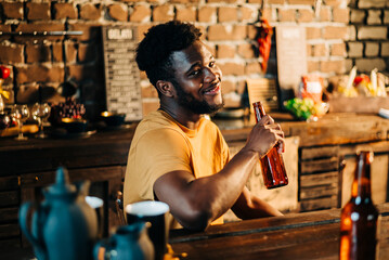 Shot of attractive african young happy smiling man drinking beer bottle in the bar close up portrait.