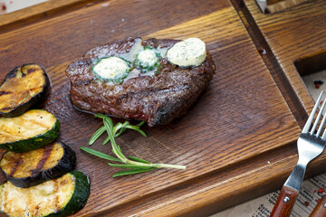 fried meat steak grilled on a wooden board with zucchini and a sprig of rosemary macro photo

