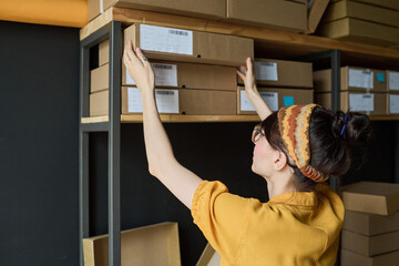 Rear view of young worker taking cardboard box from the shelf working in storage room
