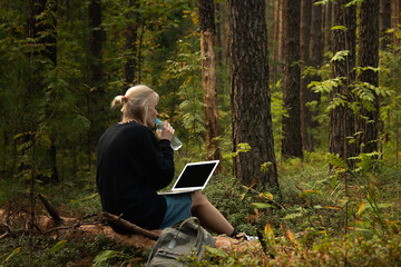 Fototapeta premium a young freelance girl is working on a laptop in the woods. remote work in nature