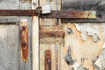 Old shabby wooden door with handle, bolt and latch. Wood surface with peeling white and beige paint texture background. Chunks of paint hang down, corrosion of metal, Rusty metal. Decay and ruins.