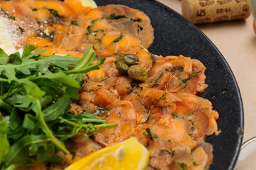 salmon carpaccio in a plate with lemon and arugula macro photo
