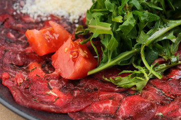 Veal carpaccio in a plate with tomatoes and arugula macro photo
