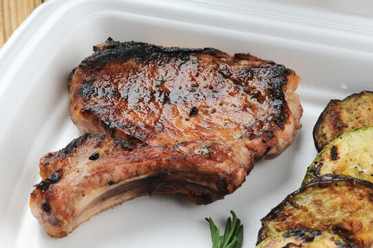 fried meat on the bone in a disposable dish with grilled zucchini
