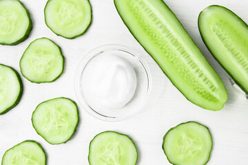 Obraz na płótnie Canvas A sample of a cosmetic product on a white wooden background with pieces of a green fresh juicy cucumber close-up. Body cream, skin treatment and nutrition.