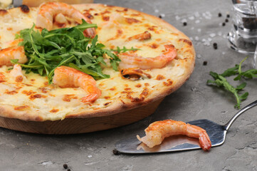 pizza with shrimp arugula and cheese on gray with a spatula
