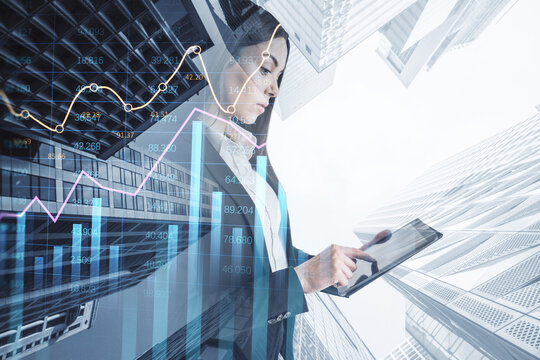 Attractive young european businesswoman using pad with creative growing financial forex chart graph on blurry city background. Market, stock and trading concept. Double exposure.