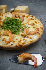 pizza with shrimp and arugula on a gray background with raw shrimp on a shoulder vertical macro photo
