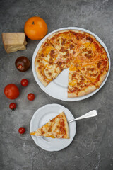 Margherita pizza on a gray background with tomatoes and cheese with a cut off slice on a separate plate vertical photo

