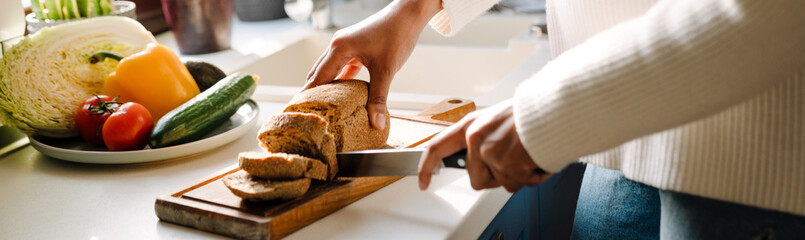 Female hands cutting bread on wooden board