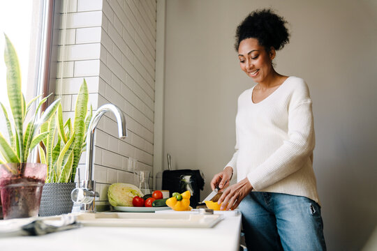 Adult beautiful smiling african woman cooking salad and cutting sweet pepper