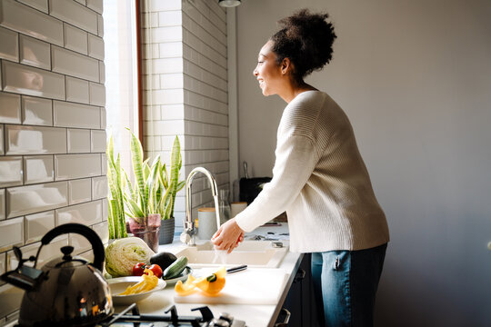 Adult beautiful african pregnant woman washing vegetables to cook salad