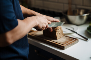 Male hands cutting bread on a wooden board closeup