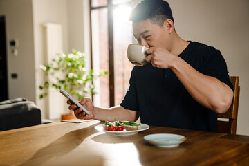 Fototapeta na wymiar Adult asian man with phone drinking tea at lunch