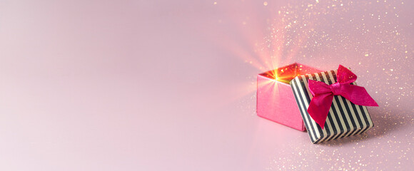 Open pink box with black stipes tap and red bow on pink background with golden spakling and light....
