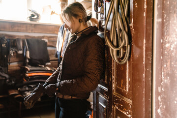 Young jockey woman preparing horse riding in stable