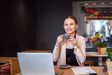 Smiling young woman using laptop at cafe while having a coffee