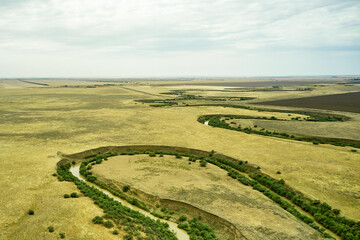 a winding muddy river with overgrown green banks in a sun-scorched steppe rural landscape