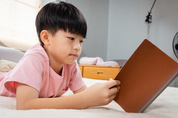 9-year-old Asian boy sitting and reading a book With pleasure, he readily reviewed the things he had learned each day in his bed in the bedroom of the house.