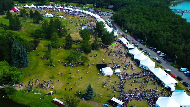 aerial view above people park tents festival mixed line ups crowds celebrating dancing eating singing performing in park by blue river thousands gather sharing in unification of love and peace harmony