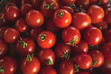 Plate full of ripe cherry tomatoes on a wooden table in sunlight