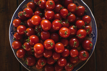 Plate full of ripe cherry tomatoes on a wooden table in sunlight