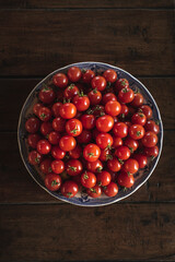 Plate full of ripe cherry tomatoes on a wooden table in sunlight