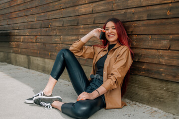 redhead smiling young girl in beige leather jacket at wall with mobile phone