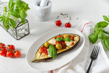 Grilled eggplant with mozzarella, cherry tomatoes, basil and olives on a plate on white background. Aubergine seasonal vegan recipe. Dieting, healthy nutrition. Restaurant menu. Side view