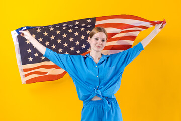 Caucasian girl. Happy young woman in blue clothes with USA flag isolated on yellow background. Independence Day. Empty space for text.