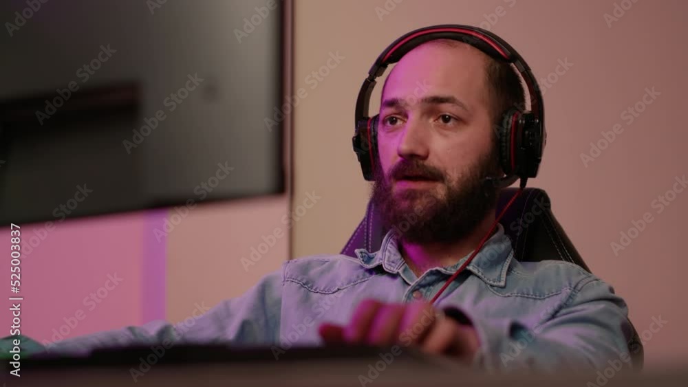 Poster handheld shot of man with gaming headset looking at computer screen and talking to team members whil
