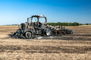 Obraz premium Feux de champs, carcasse de tracteur et d'un déchaumeur calciné suite à un incendie de chaumes lors de forte canicule
