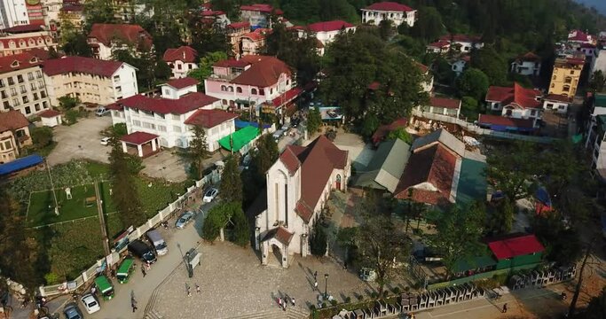 A descenting aerial shot focusing on Notre Dame Cathedral reveals a small South East Asian town in the mountains. Sapa Vietnam.