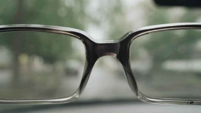 Driver of a car with poor eyesight. The driver raises his head, the silhouette of a passing car is visible through the glasses. Blurred image.