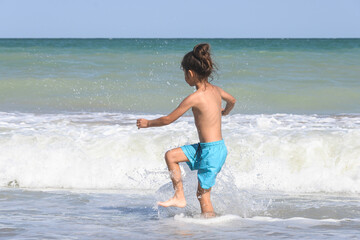Fototapeta premium The boy was enjoying the waves of the sea. A little boy with long hair is playing in the waves of the sea. 