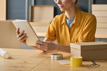 Close-up of woman using digital tablet to track parcels online at table